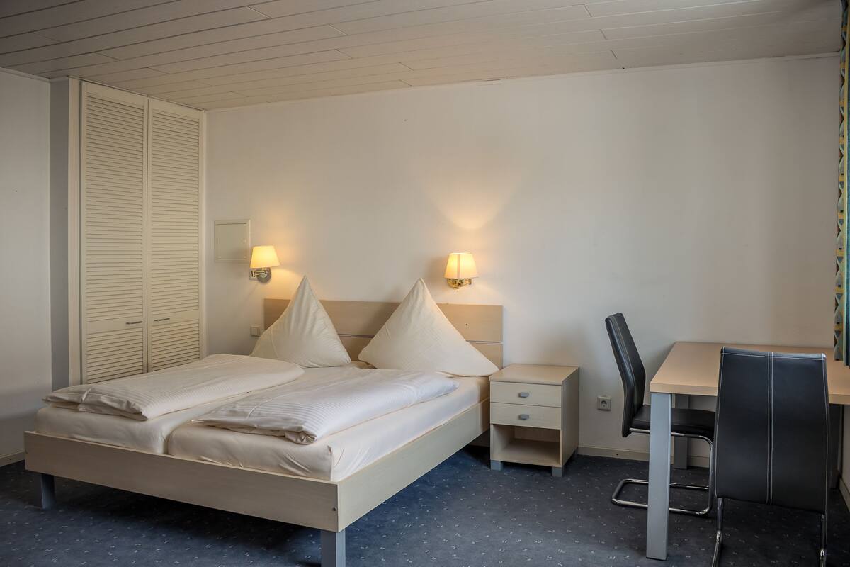 A neatly arranged hotel room with a bed, bedside tables, a desk, and a chair.