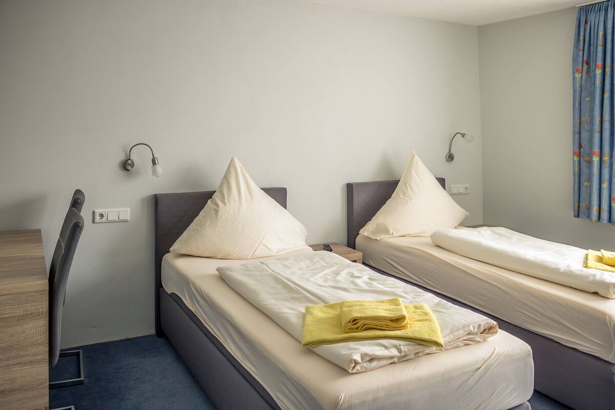 A hotel room with two single beds, a desk, and a chair.