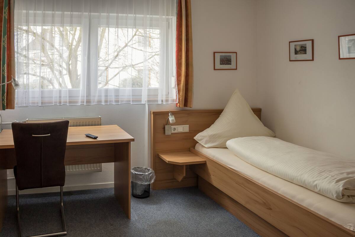 A compact room with a wooden desk, a single bed, a chair, and a radiator.