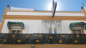 A building with a balcony decorated with sunflowers, two air conditioning units, and a green awning over the windows. - Hospedería IslaSol (San Fernando)