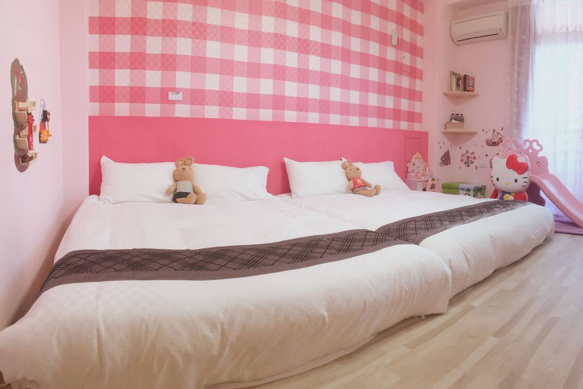 A large bed with two pillows, a teddy bear, and a Hello Kitty chair.