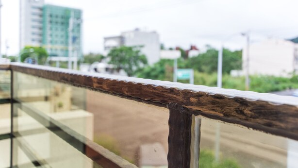 A wooden railing with a glass panel, overlooking a cityscape with buildings and greenery. - Mi Casa Bed and Breakfast (Taitung)