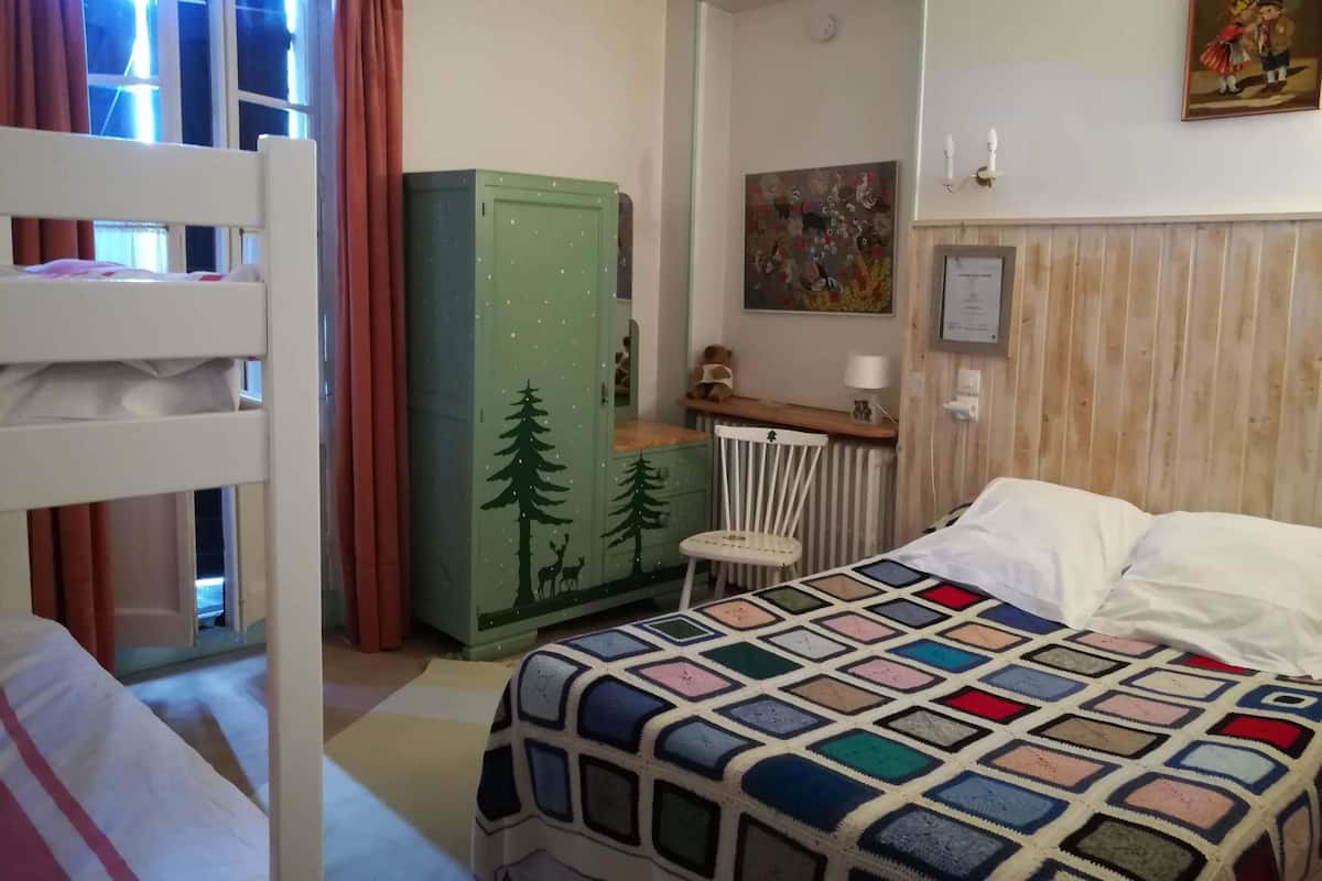 Un dormitorio con literas, un armario verde con motivos de árboles, un radiador, una silla pequeña y una manta colorida.