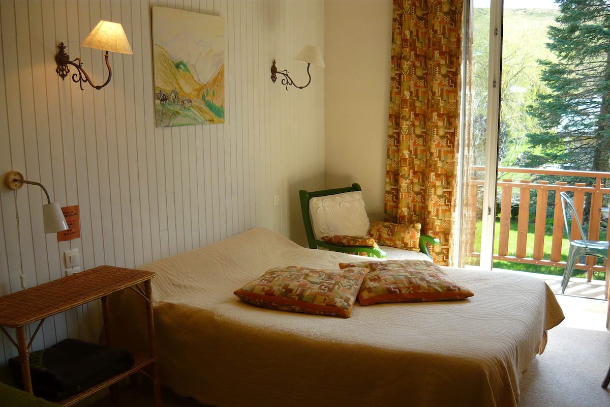 Un dormitorio con cama, dos almohadas, una silla, una mesita y un cuadro en la pared.