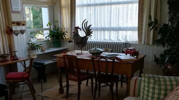 A cozy living room with a checkered sofa, a dining area with a table and chairs, and a kitchen area with a rooster decoration.