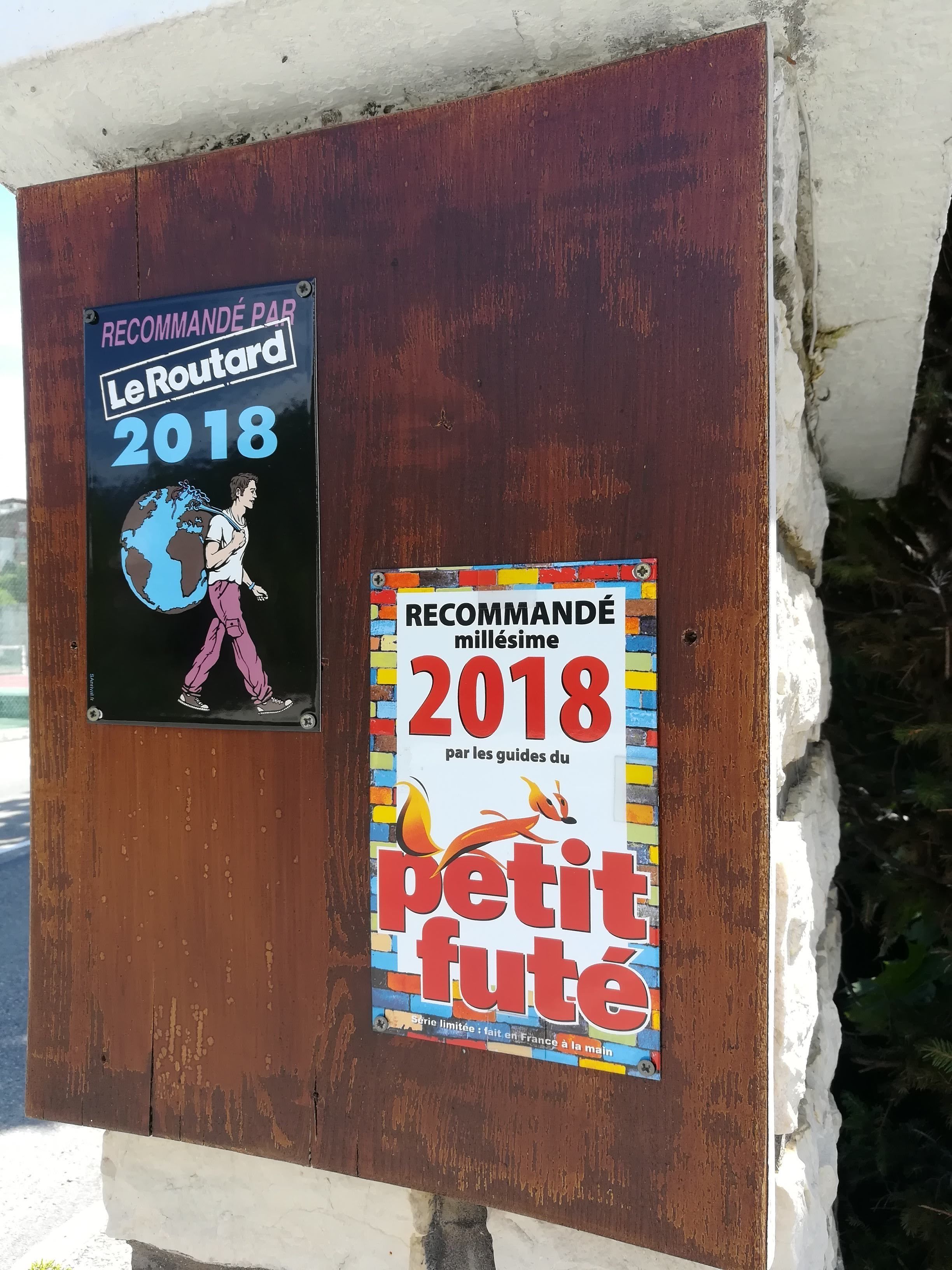 Dois cartazes fixados numa tábua de madeira desgastada, um para Le Routard 2018 e outro para a coleção Millesime Petit Fute de 2018.