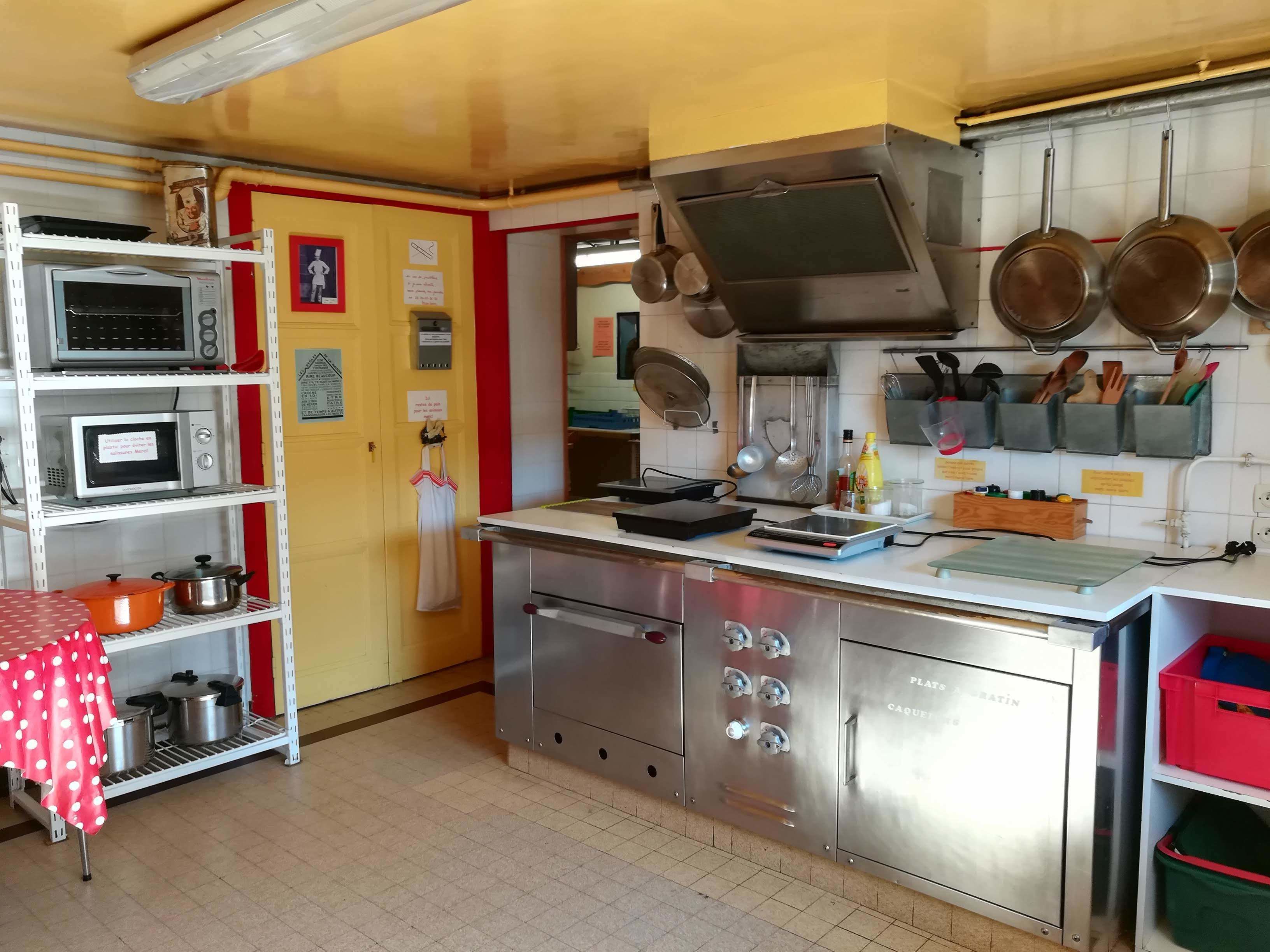 Uma cozinha com eletrodomésticos de aço inoxidável, esquema de cores vermelho e amarelo, e diversos utensílios e panelas.