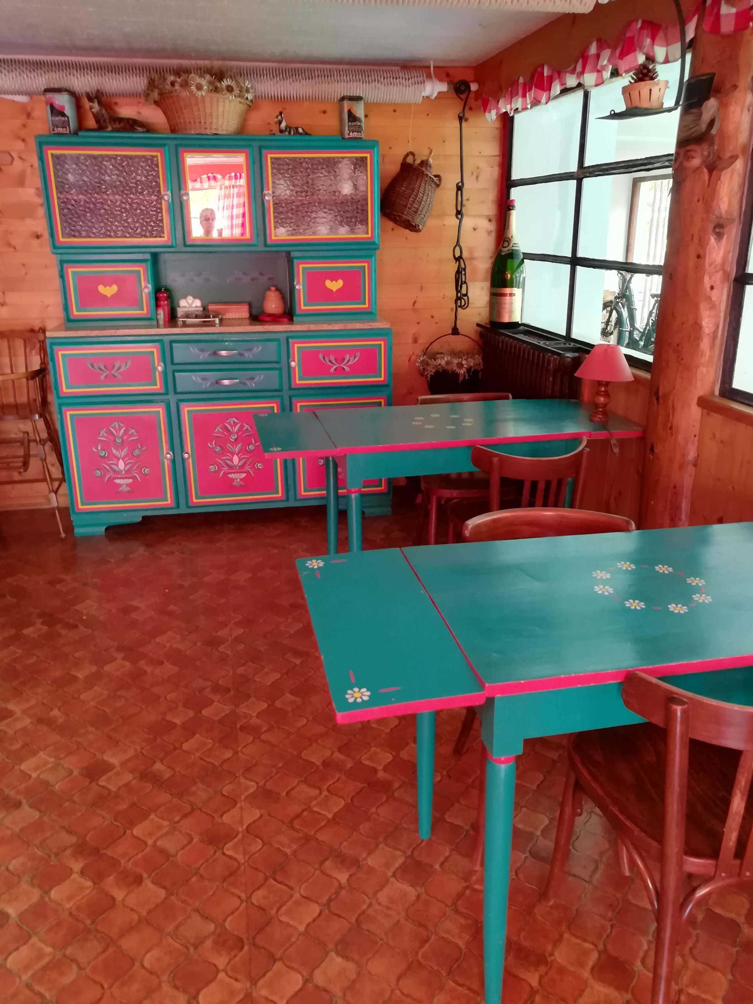 Una cocina rústica con armarios de madera, una mesa color turquesa y una ventana con vista a bicicletas.