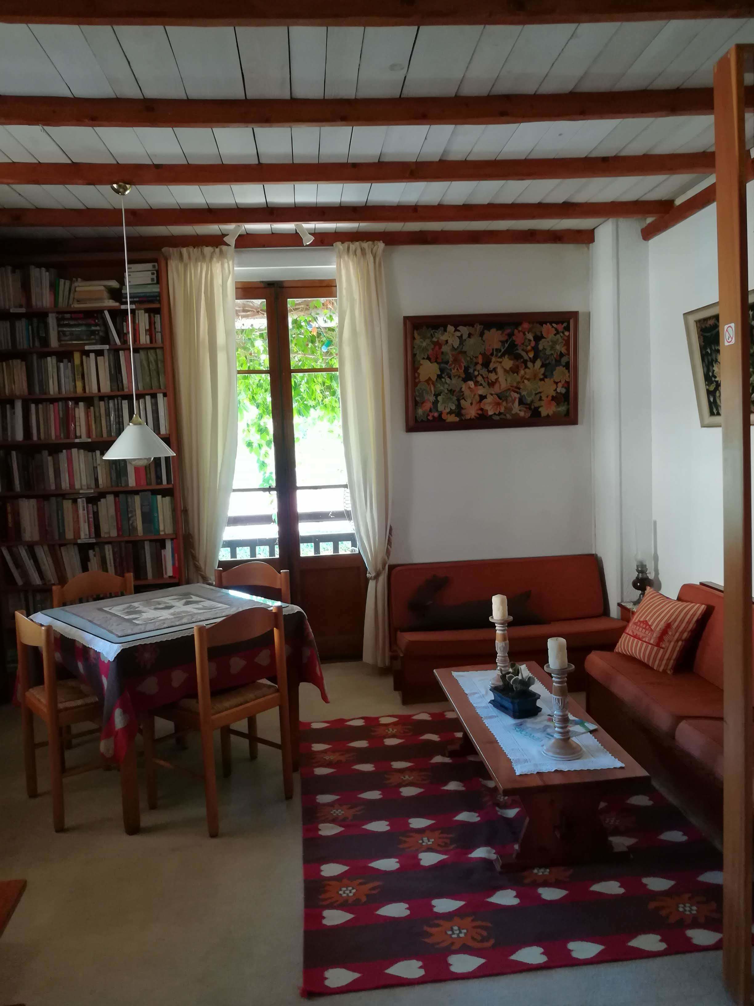 A cozy living room with a wooden ceiling, a bookshelf, a sofa, a dining table, and a patterned rug.