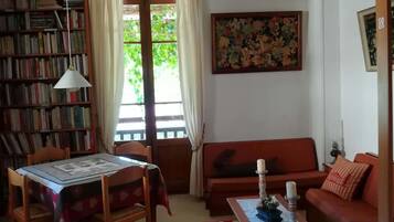 A cozy living room with a wooden ceiling, a bookshelf, a sofa, a dining table, and a patterned rug.