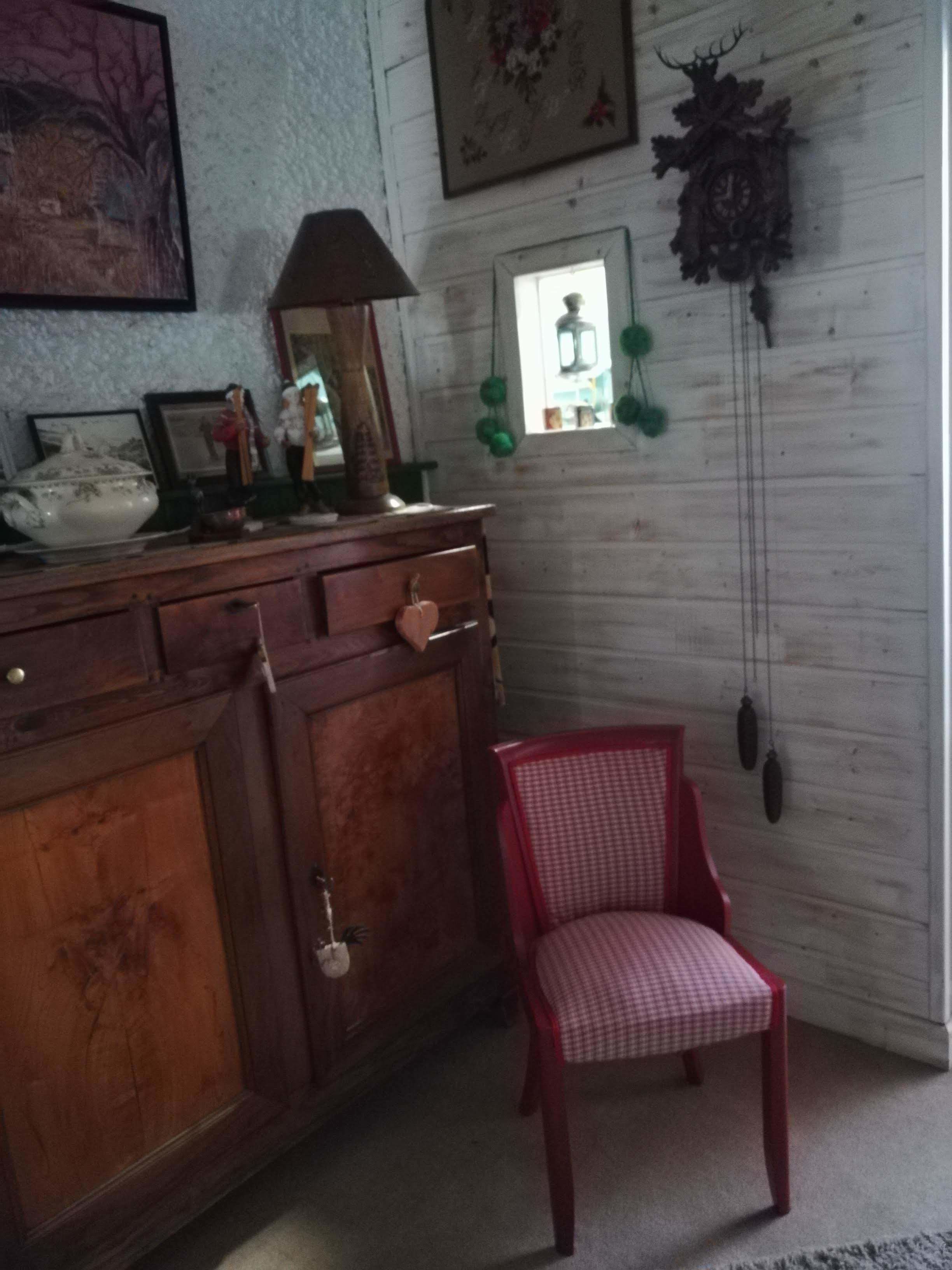 A wooden dresser with a mirror, a red chair, and wall-mounted decorations including a clock and a framed picture.