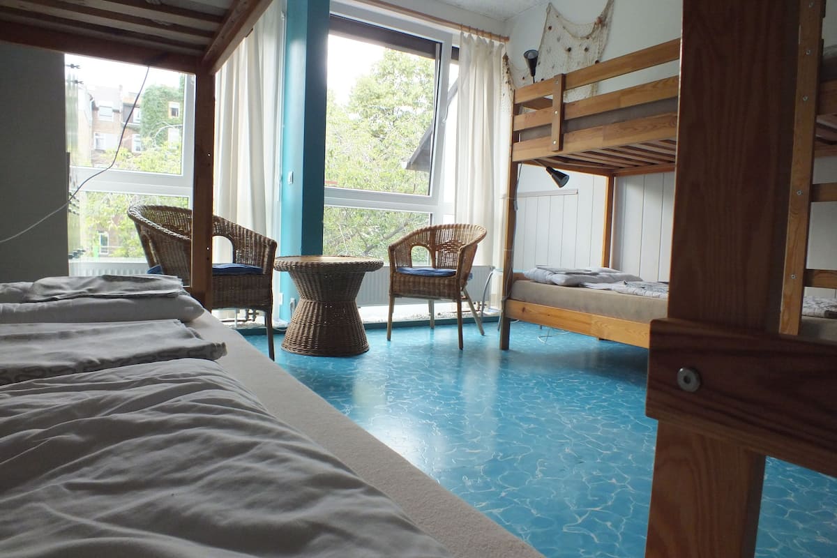 A room with bunk beds, a table, two chairs, and a view of the outside.