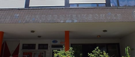 A building with a flat roof, large windows, and a covered entrance area with a sign that reads "Hostel."