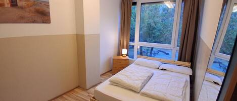 A bedroom with a wooden bed, a nightstand, a lamp, and a large window with curtains.