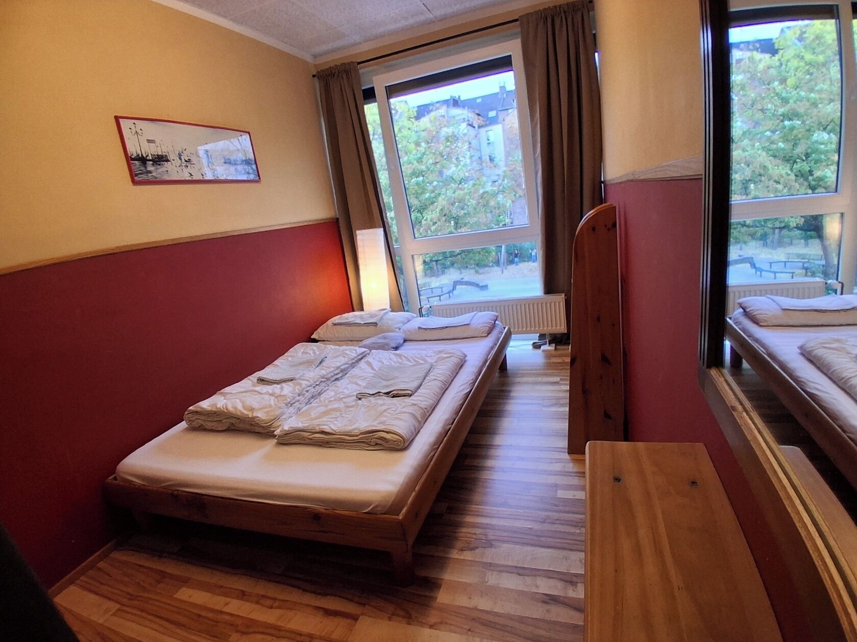 Una habitación con dos camas, suelo de madera, una ventana con cortinas y un radiador.
