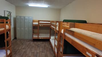 Un dormitorio con literas, suelo de madera, taquillas y una luz fluorescente.