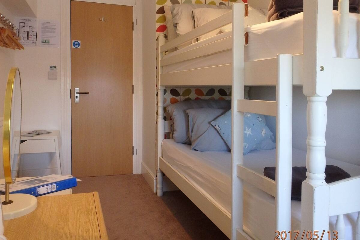 A bunk bed room with a wooden door, a small desk with a chair, and a wall with a colorful pattern.