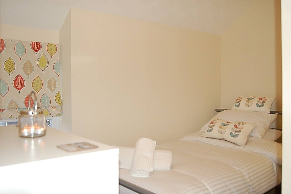 A hotel room with a bed, pillows, a bedside table, and a wall with a leaf pattern.