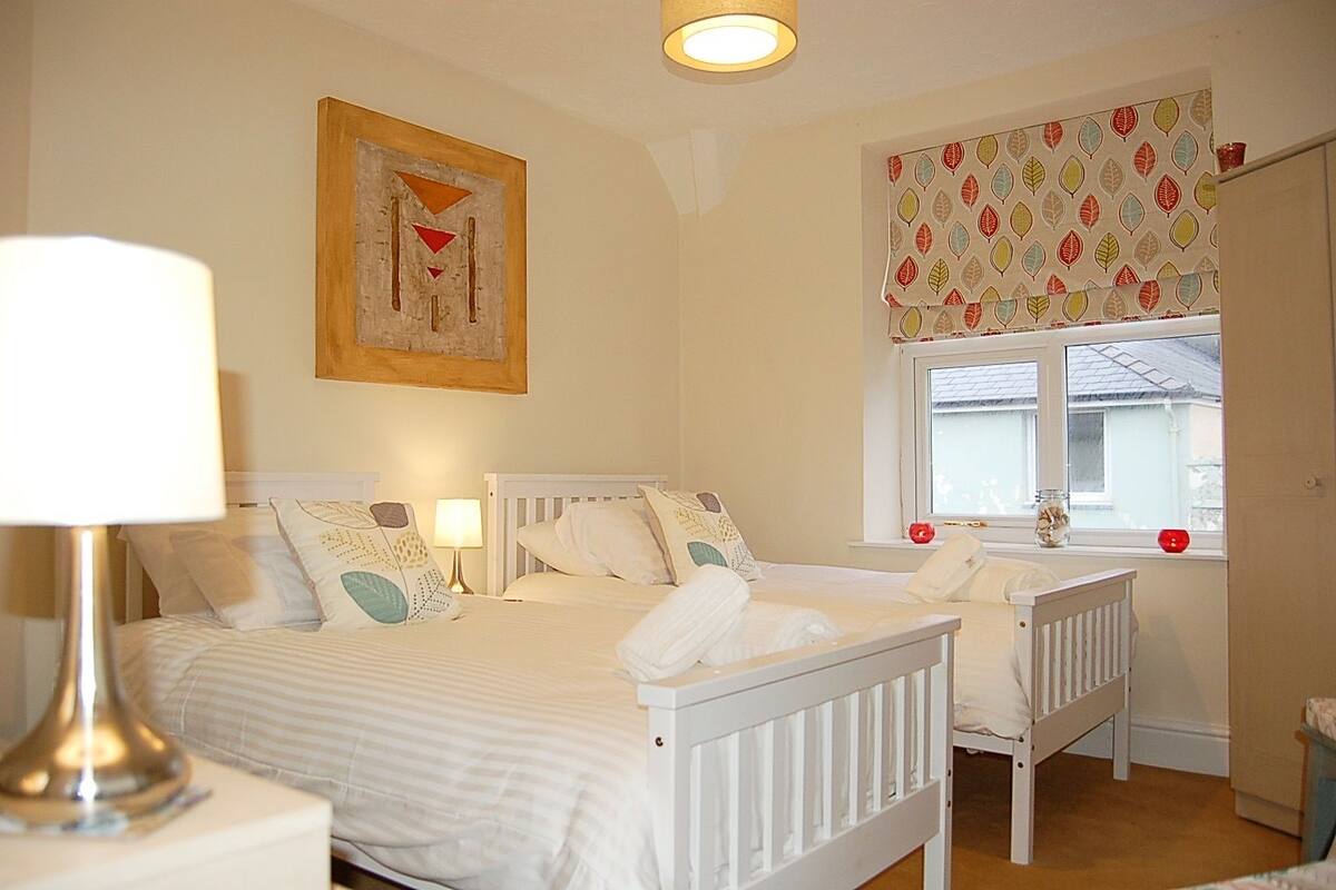A bedroom with two beds, a window with patterned curtains, and a painting on the wall.