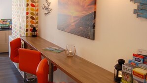 A modern room with a wooden table, orange chairs, a painting, and a wall with a leaf pattern. - Saint Cadfans Lodge (Tywyn)