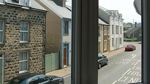 A window with a view of a street, stone buildings, and parked cars. - Saint Cadfans Lodge (Tywyn)
