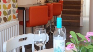 A dining area with a table set for two, a bottle of wine, and a vase with flowers. - Saint Cadfans Lodge (Tywyn)