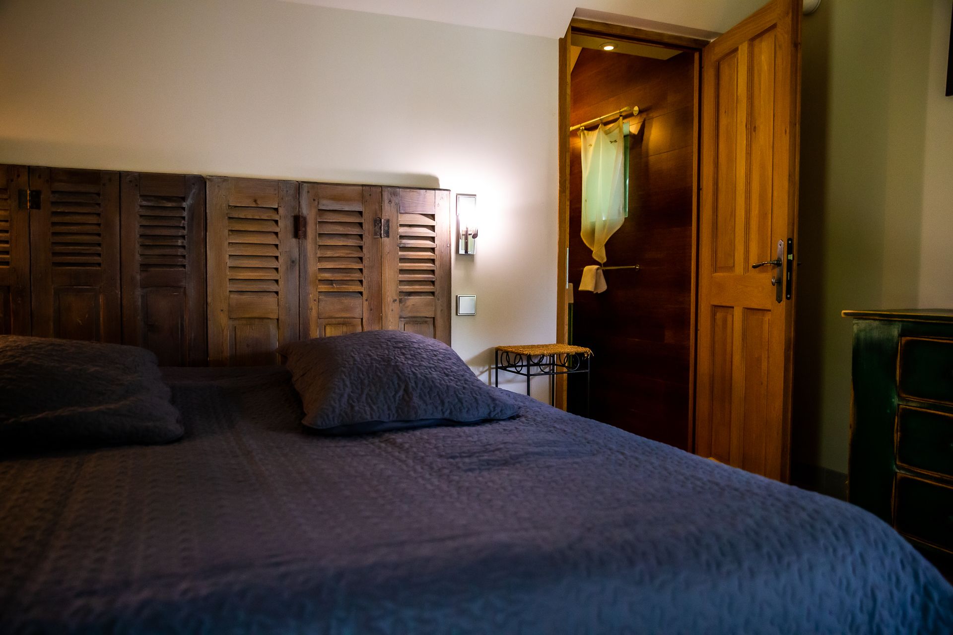 Ein Schlafzimmer mit einem großen Bett, einem Holz-Kopfteil, einem kleinen Tisch und einer Tür zu einem weiteren Raum.