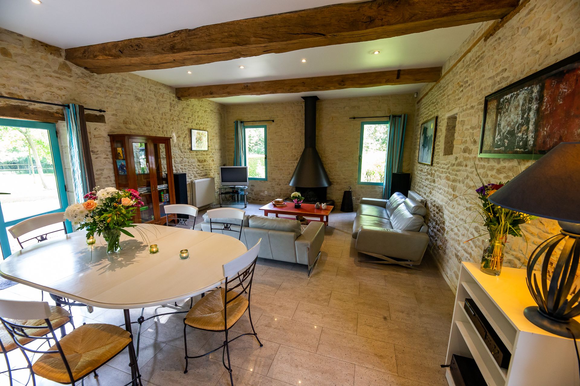 A spacious living area with a stone wall, wooden beams, a fireplace, and a dining table with chairs.