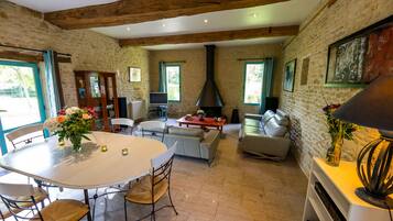 A spacious living area with a stone wall, wooden beams, a fireplace, and a dining table with chairs.
