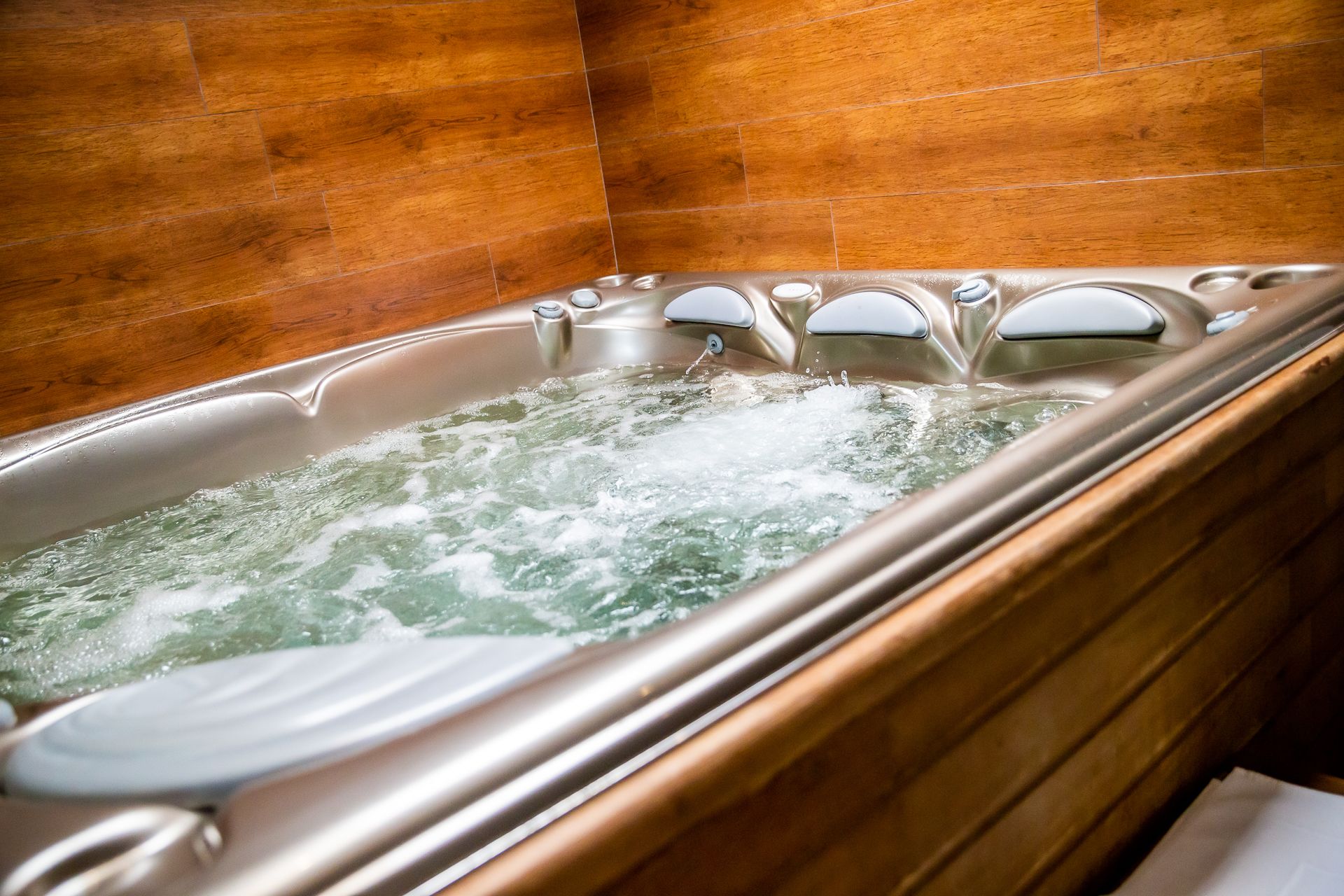 A hot tub with a wooden interior and a tiled wall.