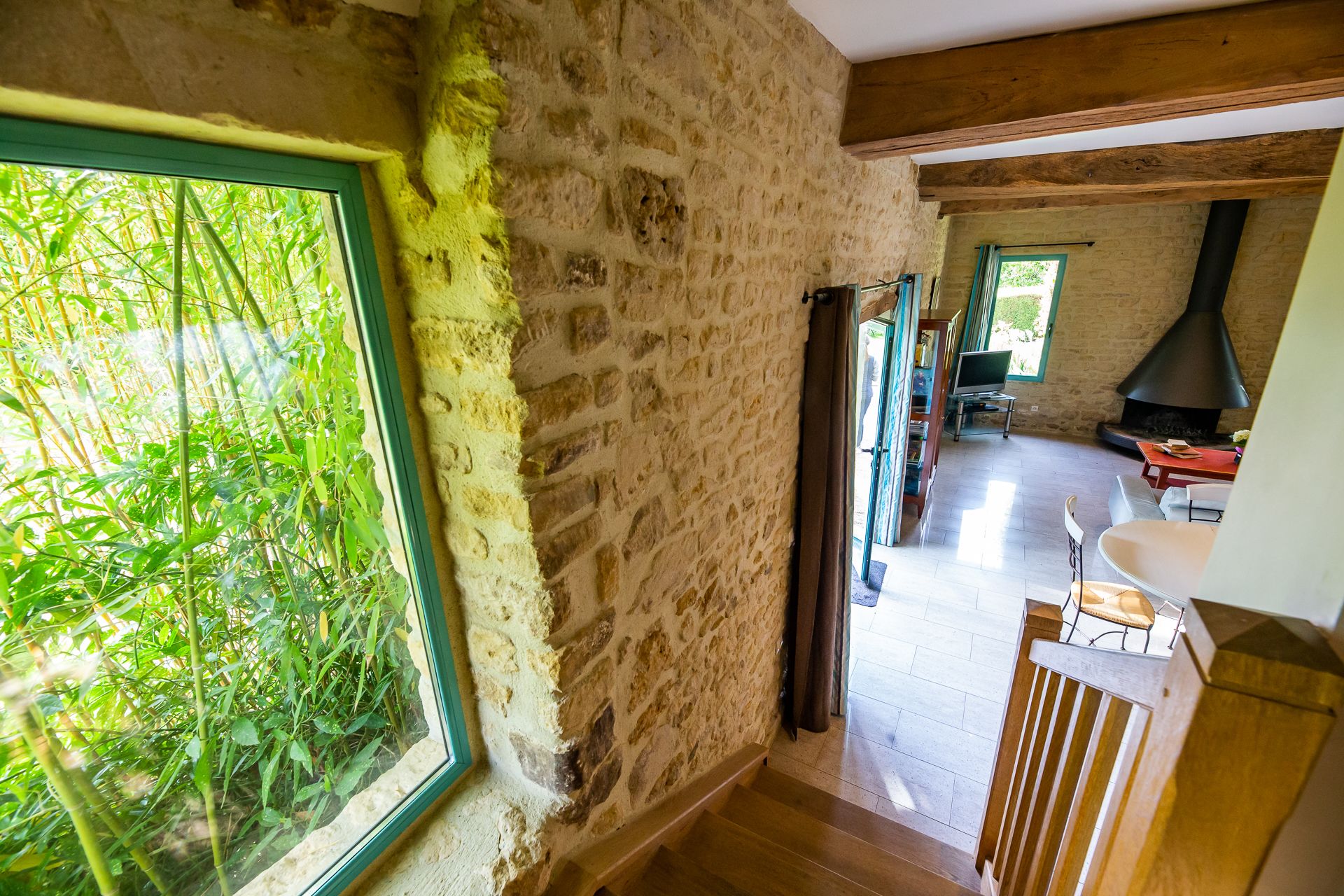 A rustic interior with stone walls, a wooden staircase, and a view of greenery outside.