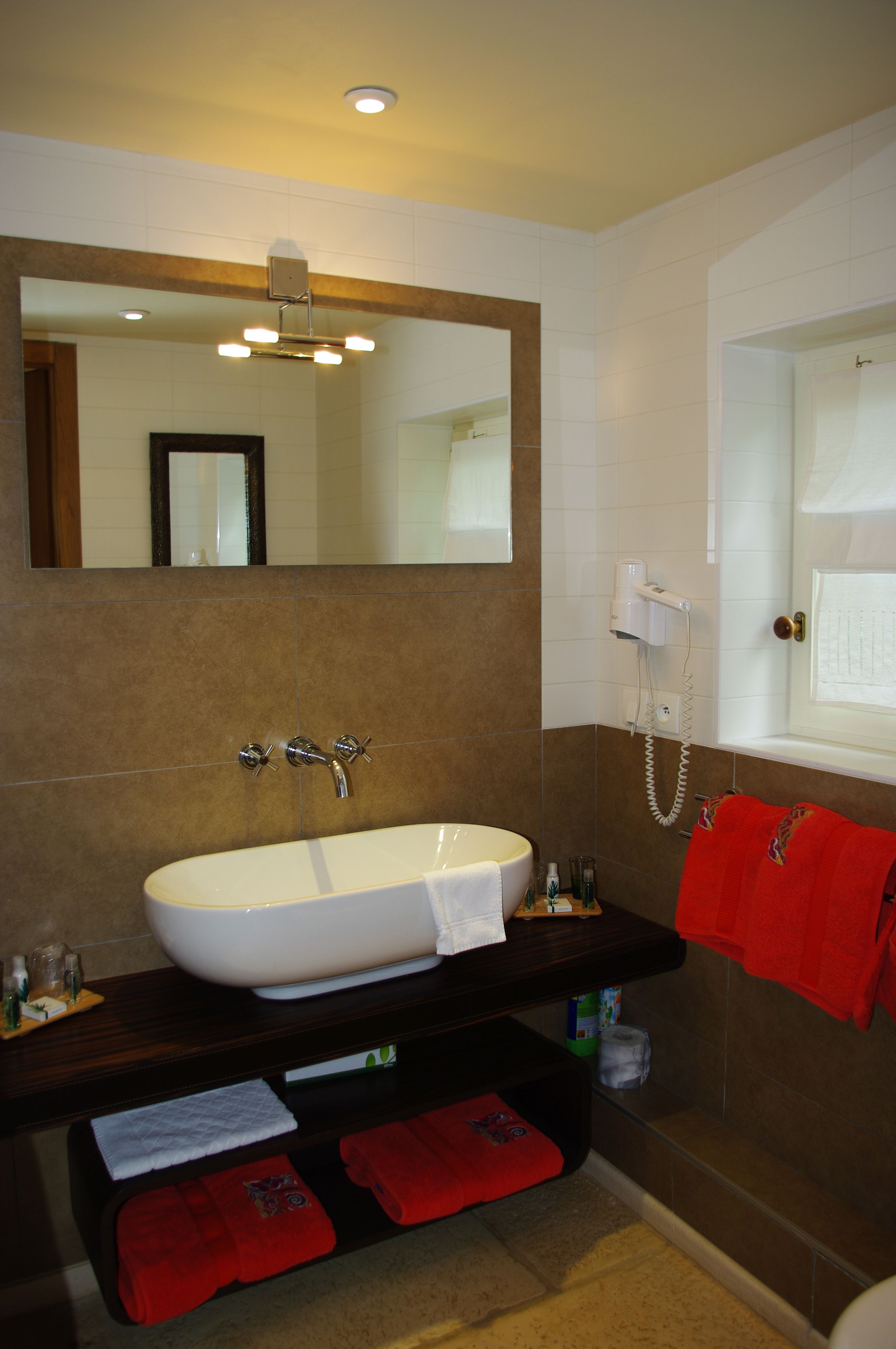 A bathroom with a large white sink, a mirror above it, and a red towel hanging on the wall.