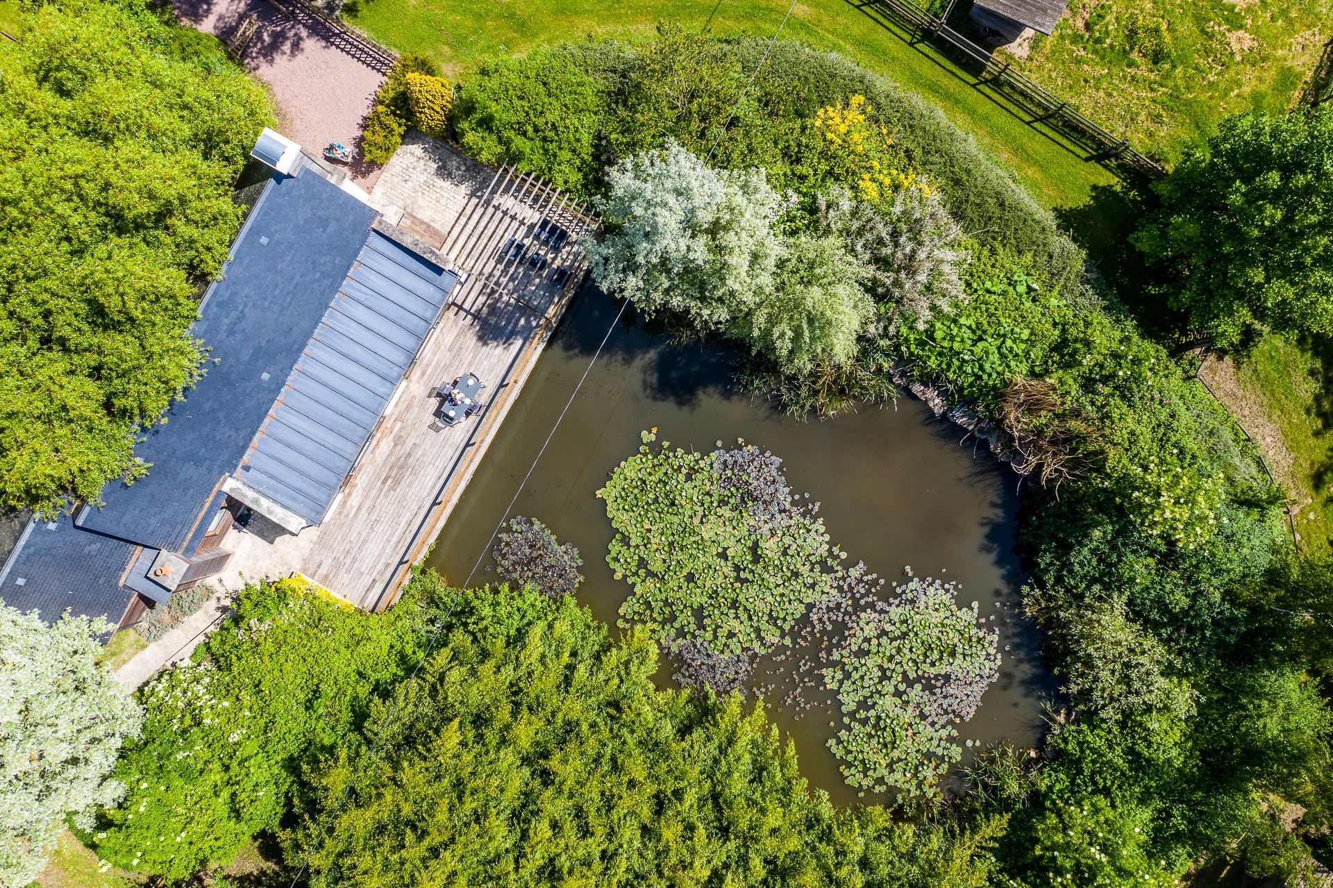 An aerial view of a riverside property with a dock, a covered seating area, and lush greenery.