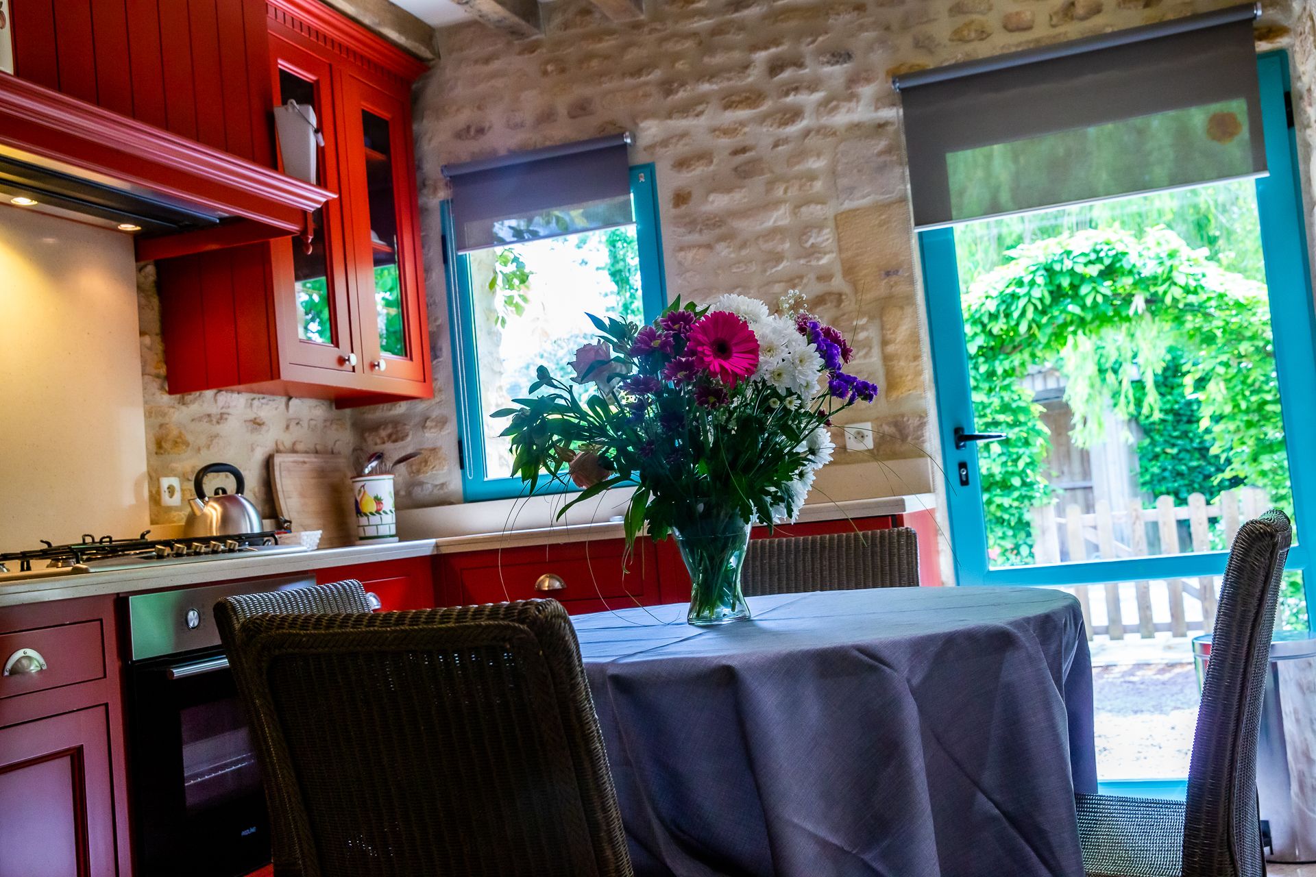 A kitchen with red cabinets, a gas stove, and a dining area with a table and chairs.
