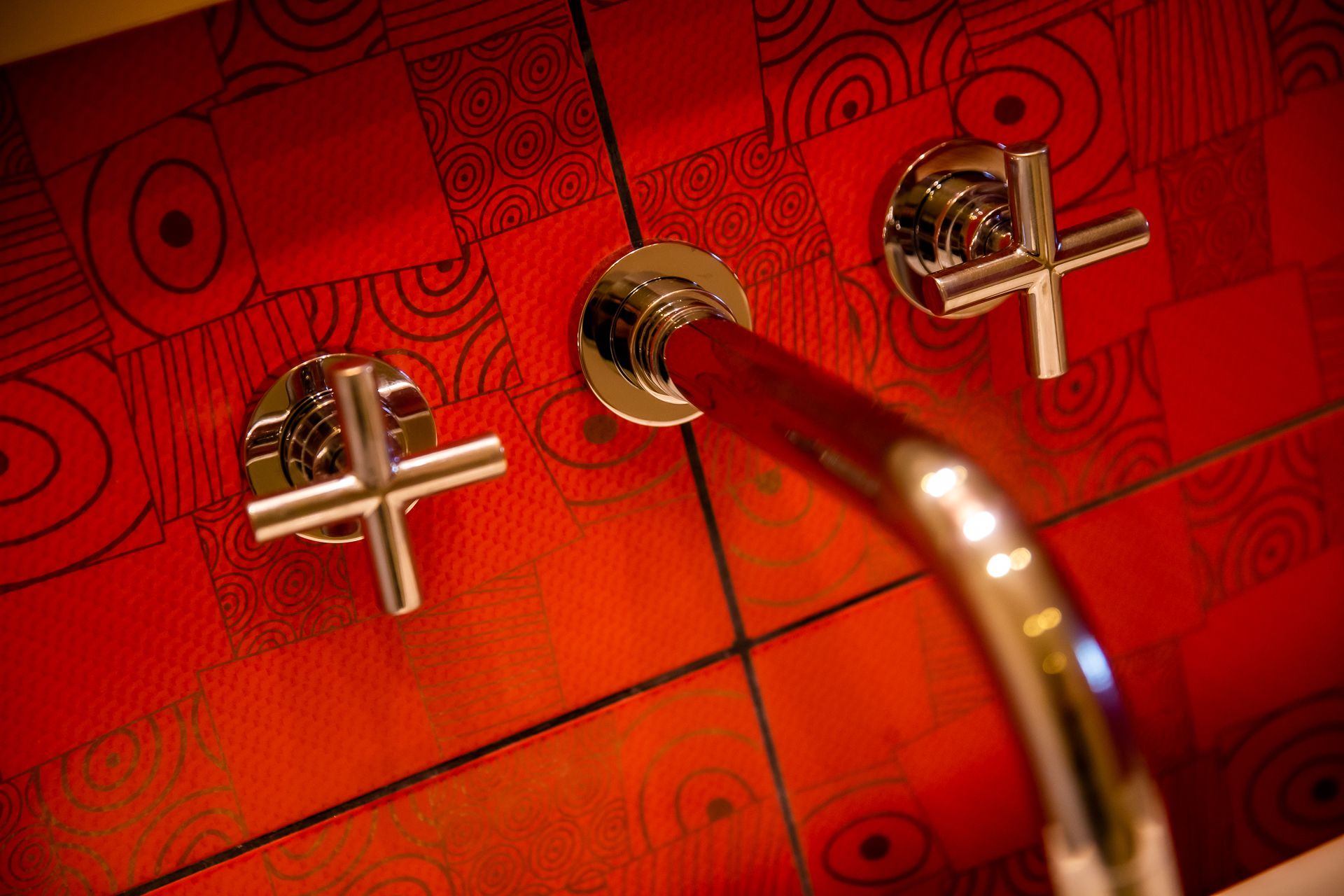 A bathroom with a red patterned tile wall and a chrome faucet.