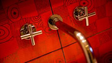 A bathroom with a red patterned tile wall and a chrome faucet.