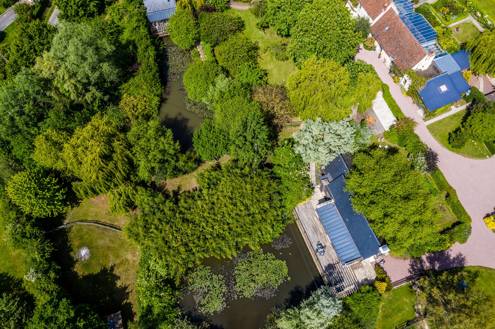 Oversigtsbillede af en ejendom med en flod, frodig vegetation og en bygning med et blåt tag.