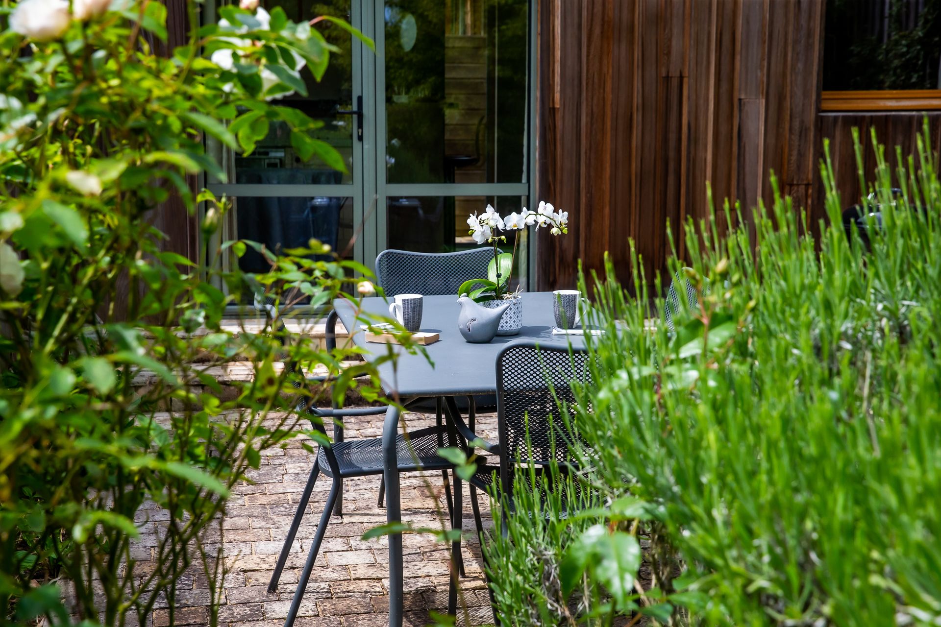 Une terrasse extérieure avec une table et des chaises, entourée de verdure et d’une clôture en bois.