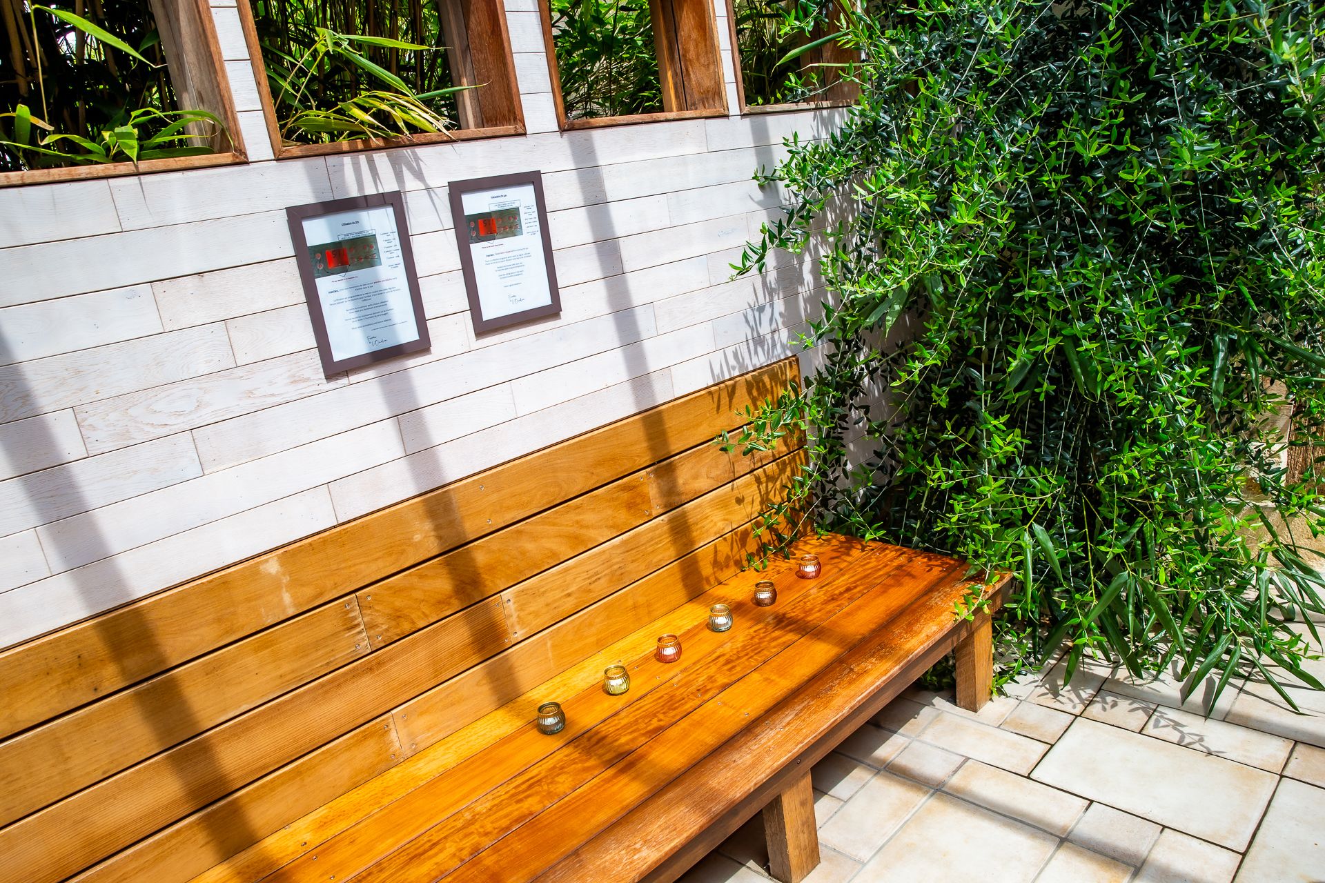 A wooden bench with a white wall behind it, featuring two framed informational signs.