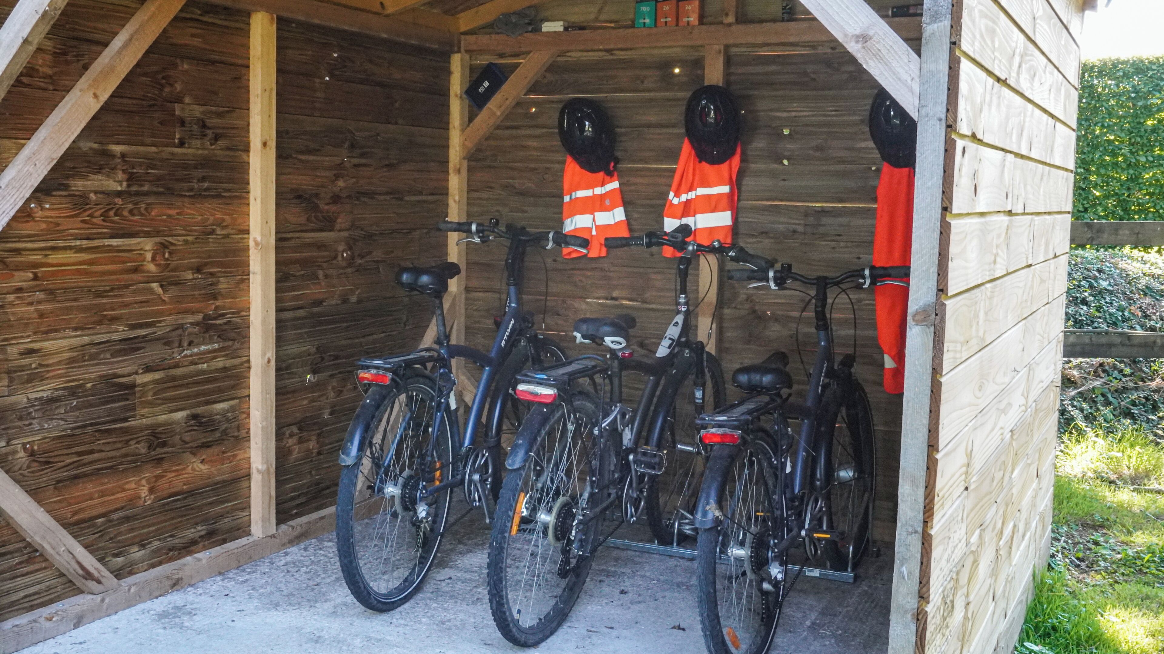 Un cobertizo de madera con tres bicicletas estacionadas en su interior, cada una con un casco colgado en la pared.
