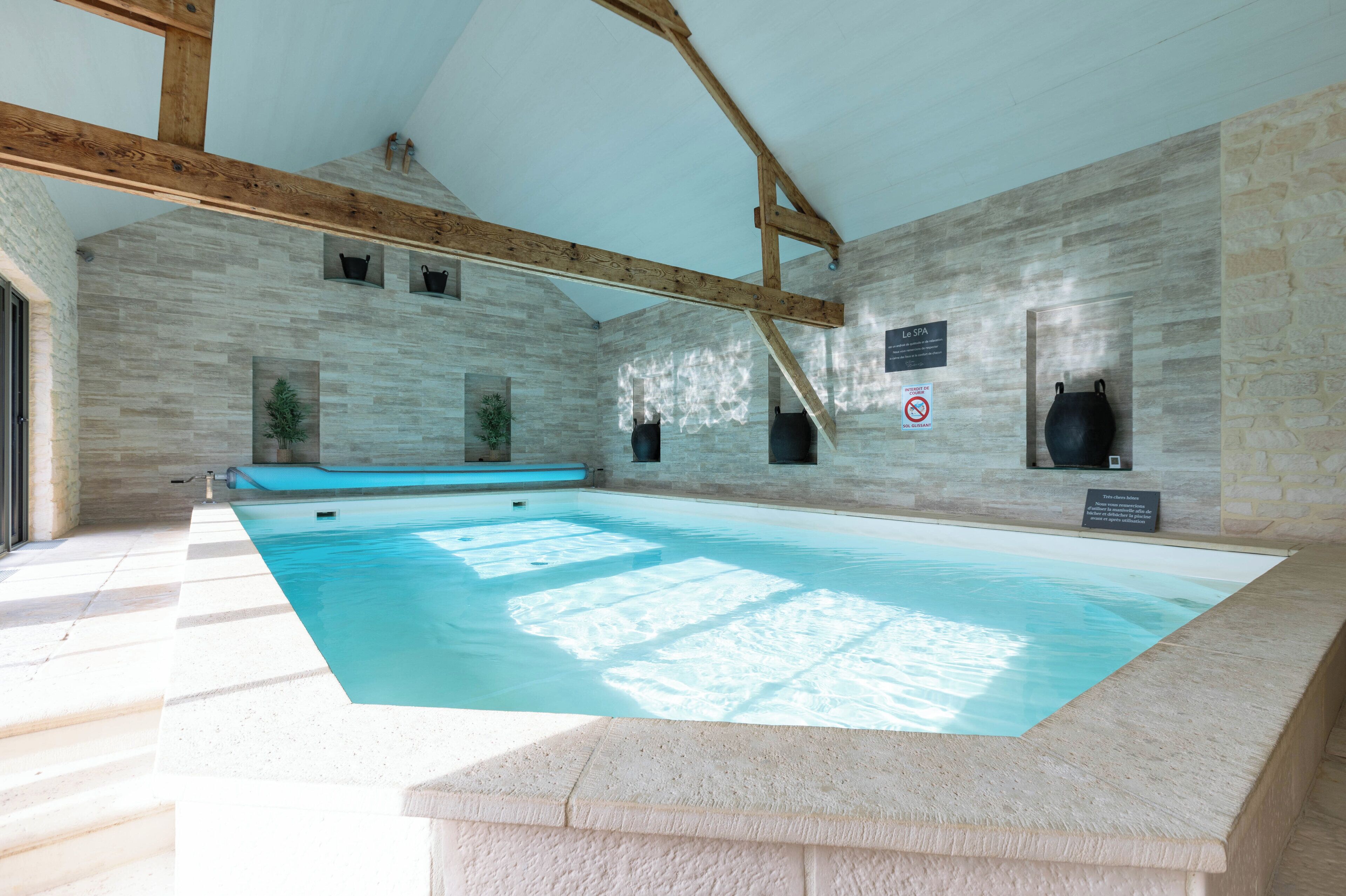 A large indoor swimming pool with stone walls and wooden beams, a spa sign, and a no smoking sign.