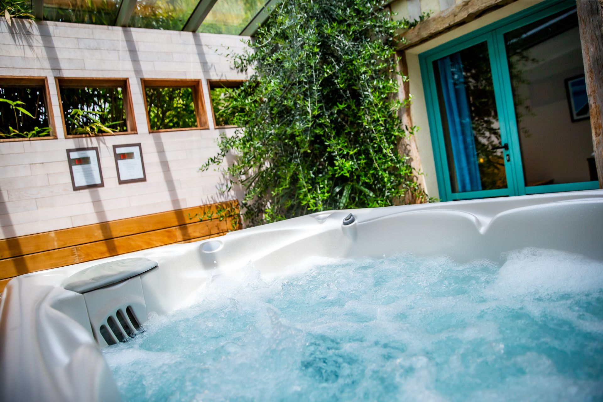 A hot tub with water bubbling, surrounded by a building with a tiled wall and windows.