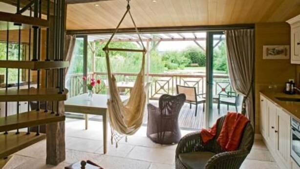 A room with a wooden ceiling, a hammock, wicker chairs, a dining table, and a view of greenery outside. - Maison d'Hôtes La Ferme de L'Oudon & Spa (Saint-Pierre-en-Auge)