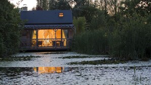 A wooden cabin with a balcony, surrounded by water and vegetation. - Maison d'Hôtes La Ferme de L'Oudon & Spa (Saint-Pierre-en-Auge)