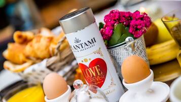 A breakfast setting with a can of plantami infusions, eggs, a glass of orange juice, and a basket of pastries.