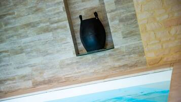 A black vase on a glass shelf against a textured wall.
