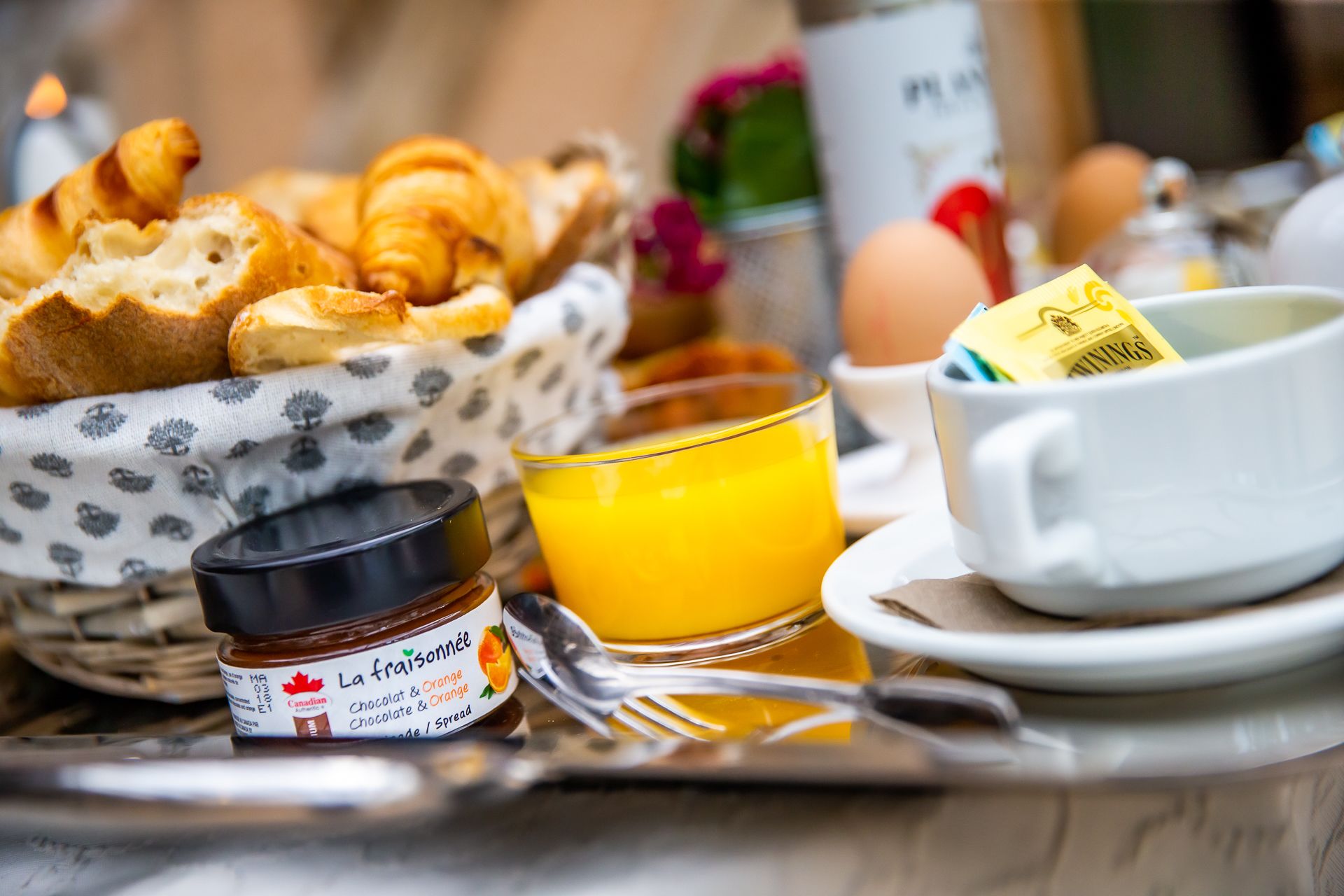 Bandeja de desayuno con croissants, un vaso de zumo de naranja, un tarro de crema de chocolate y naranja, y una taza de café.