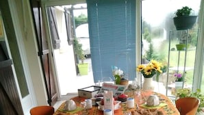 A round table with a floral tablecloth, orange chairs, and various breakfast items. - Chambres d'hôtes Maison Entre Terre et Mer (Primelin)