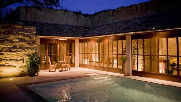 A poolside area with a stone wall, a pool, and a seating area with chairs and a table. - Château Latour Segur Suites & Spa (Lussac)