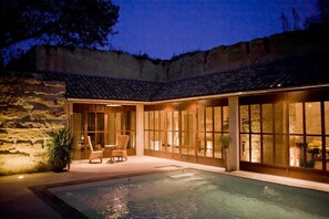 A poolside area with a stone wall, a pool, and a seating area with chairs and a table.